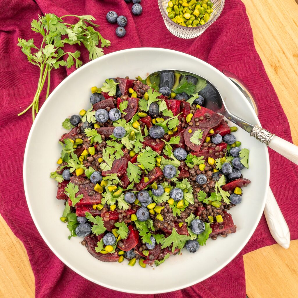Blick von oben in eine Schüssel mit Rote Bete-Linsen-Salat mit Blaubeeren und Pistazien, bestreut mit Koriandergrün.