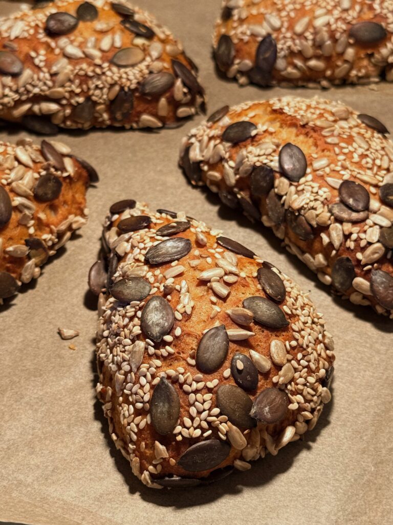 Blick auf ein Blech voller knusprig brauner Körnerbrötchen in dreieckiger Form.